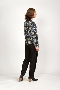 Woman in abstract print long sleeve blouse, black trousers, and ankle boots, side view