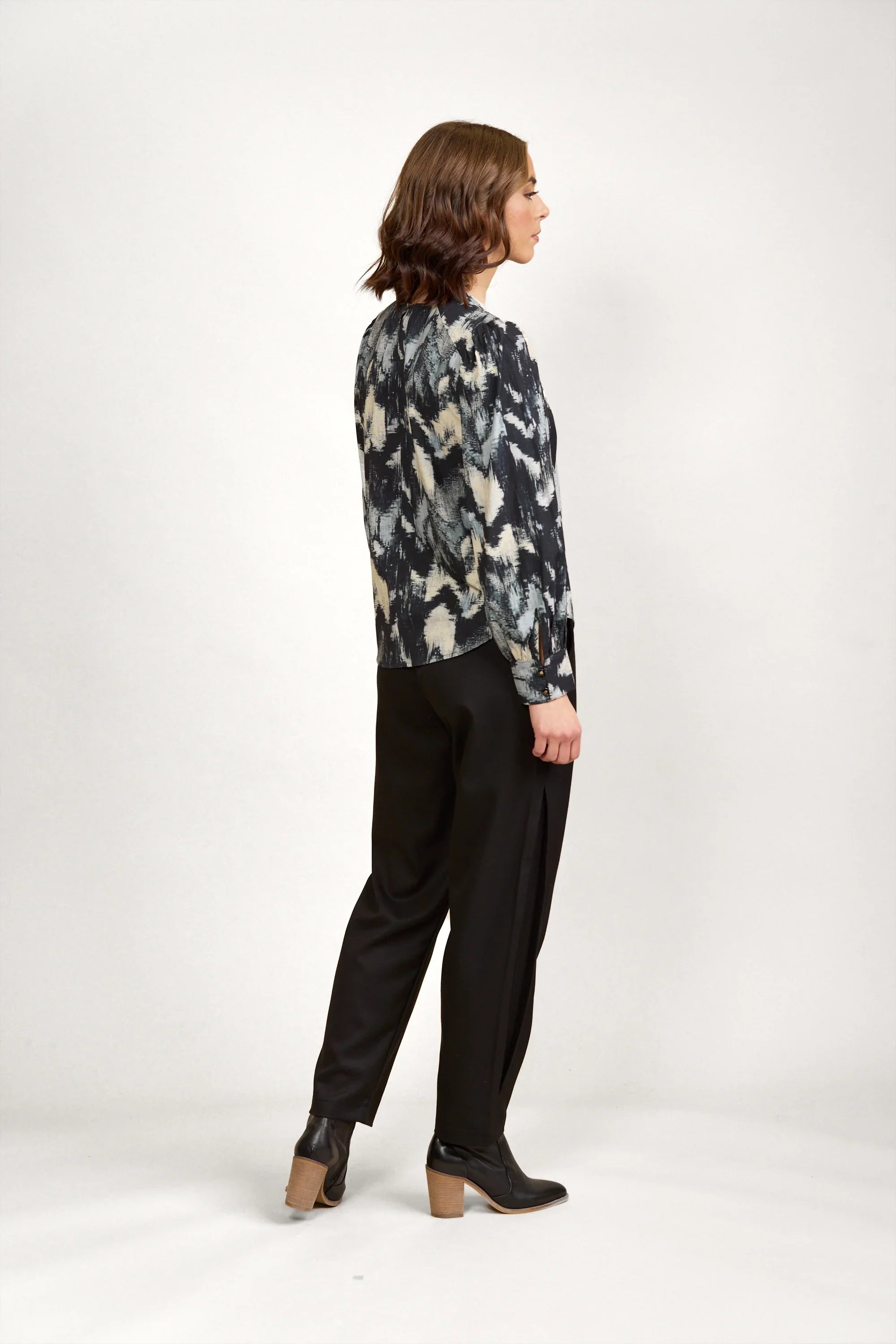 Woman in abstract print long sleeve blouse, black trousers, and ankle boots, side view