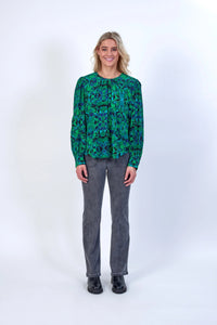 Woman wearing a green patterned long sleeve blouse with grey jeans and black boots