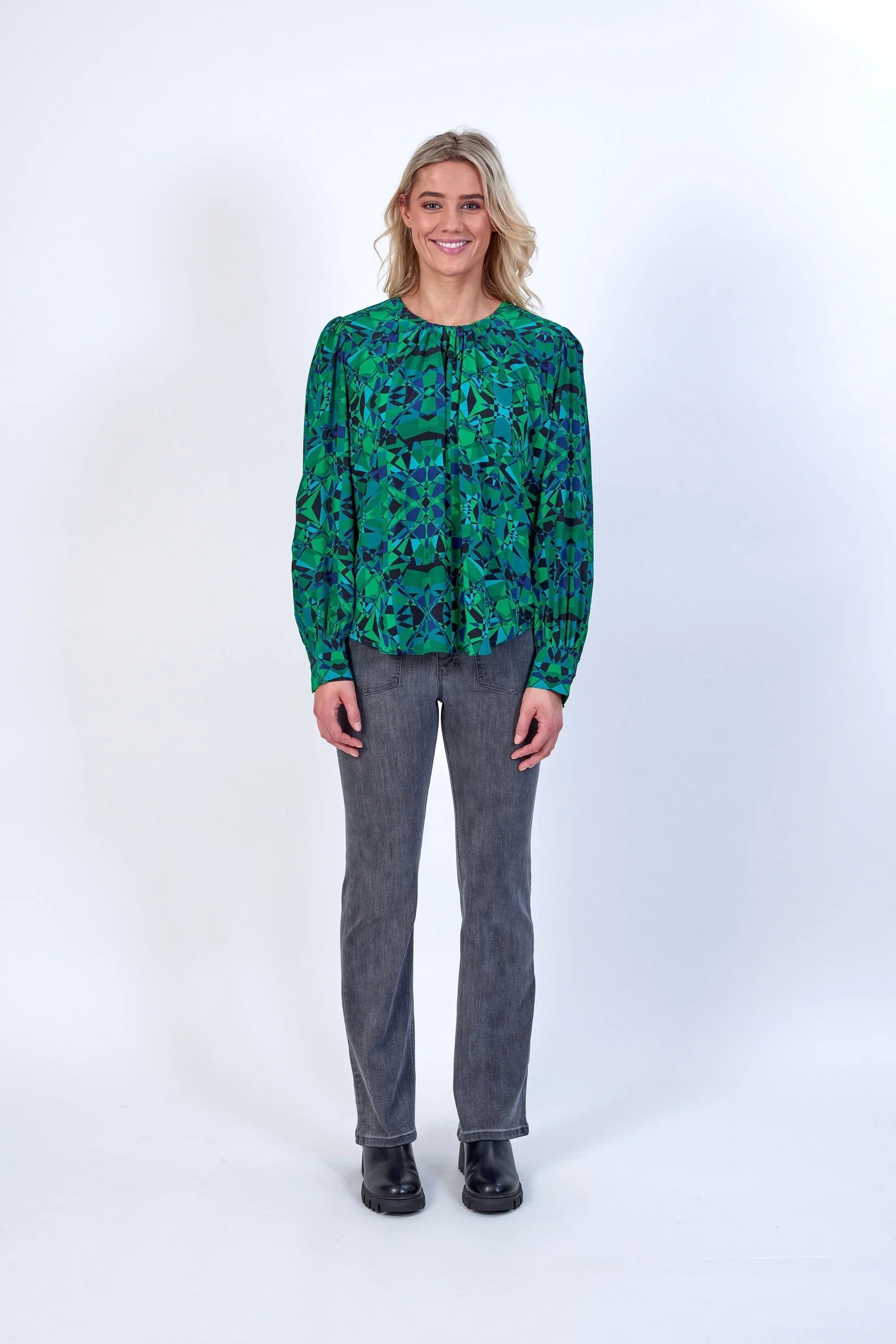 Woman wearing a green patterned long sleeve blouse with grey jeans and black boots