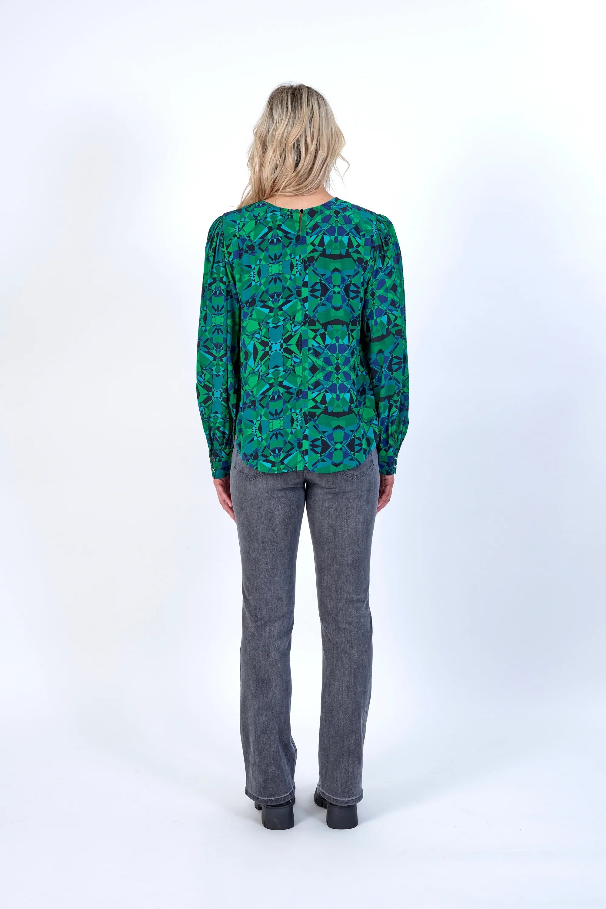 Woman wearing a green geometric print long sleeve blouse and grey jeans, back view
