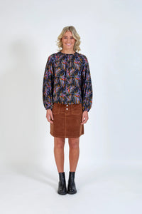 Woman wearing a colorful long-sleeve blouse, brown corduroy skirt, and black boots