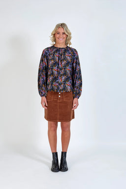 Woman wearing a colorful long-sleeve blouse, brown corduroy skirt, and black boots