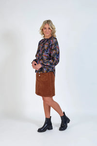 Woman wearing a long-sleeve printed blouse, brown corduroy skirt, and black boots