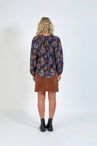 Woman in a colorful floral print blouse, brown corduroy skirt, and black ankle boots, back view
