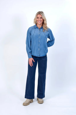 Woman wearing a blue denim button-up shirt with long sleeves and dark wide-leg jeans