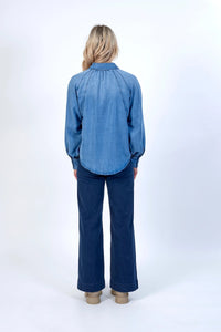 Woman wearing blue denim long sleeve shirt and wide-leg jeans, photographed from the back.
