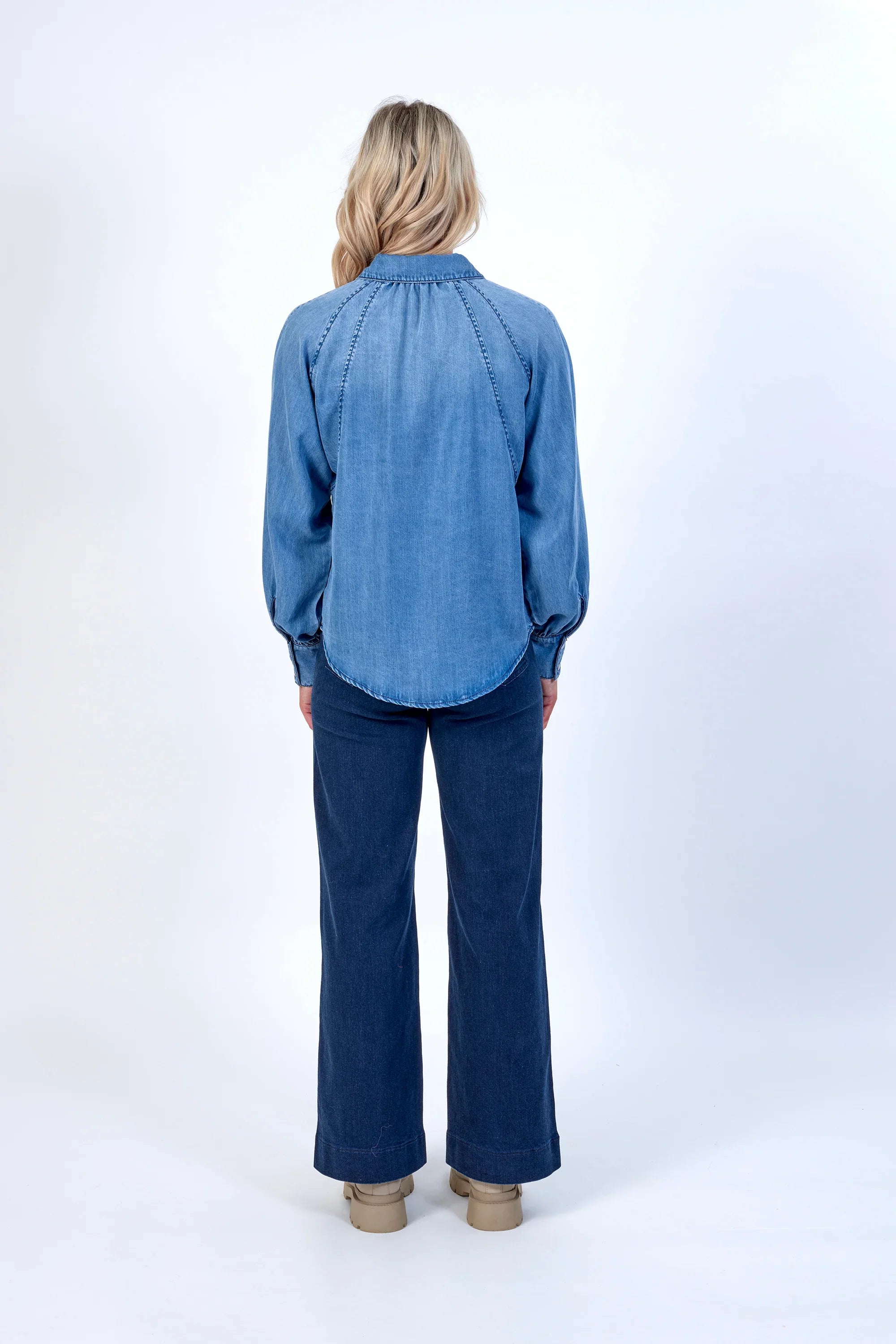 Woman wearing blue denim long sleeve shirt and wide-leg jeans, photographed from the back.