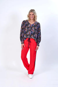 Woman wearing a long sleeve floral blouse with vibrant red high-waisted pants and white sneakers