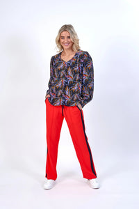 Woman in a multicolored long-sleeve blouse and red wide-leg pants with black side stripes
