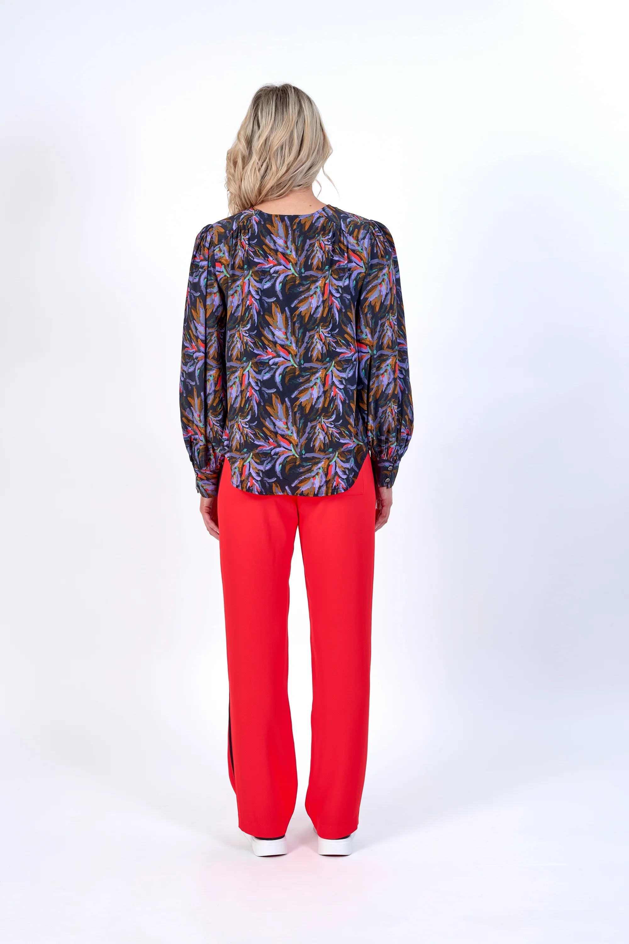 Woman wearing long sleeve floral blouse with red wide-leg pants, back view