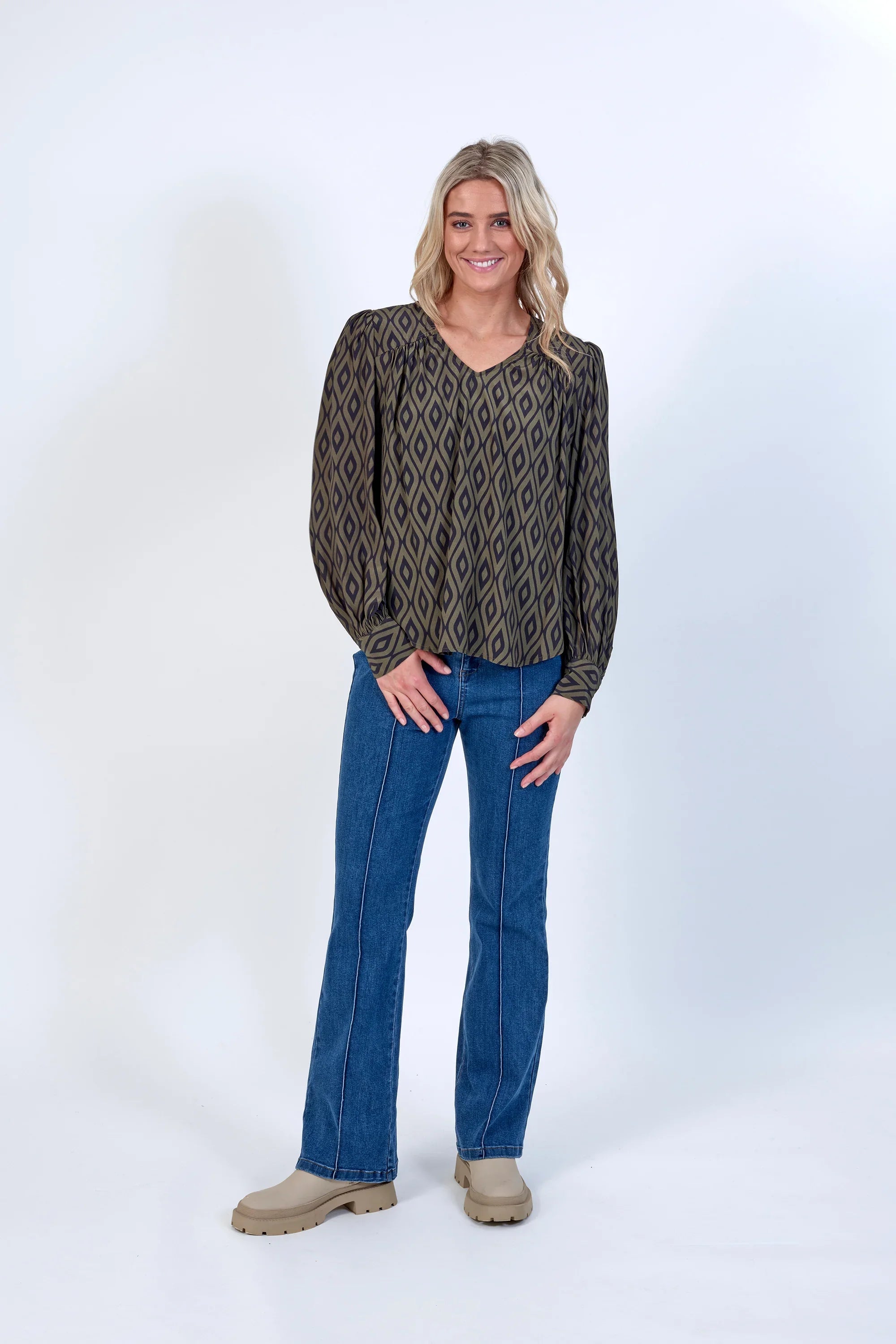 Woman wearing geometric print blouse with long sleeves, blue jeans, and beige boots
