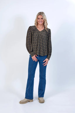 Woman wearing geometric print blouse with long sleeves, blue jeans, and beige boots