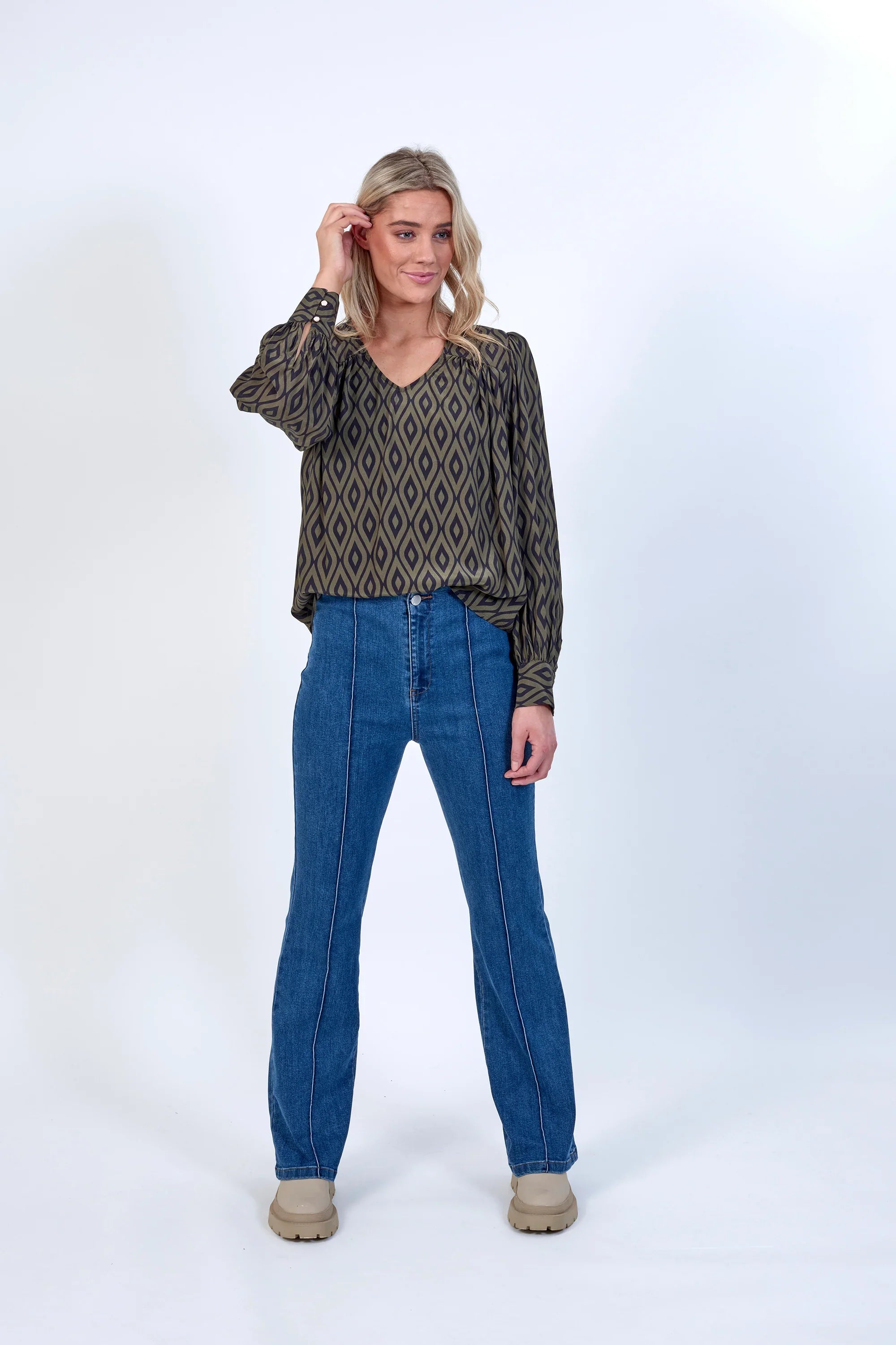 Woman wearing patterned long-sleeve blouse with blue straight-leg jeans, neutral background