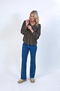 Woman wearing geometric print blouse with puff sleeves, blue jeans, and beige boots