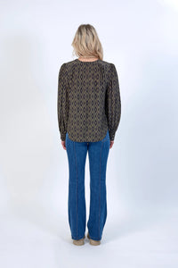 Woman wearing geometric print long sleeve blouse and blue jeans, back view, studio setting