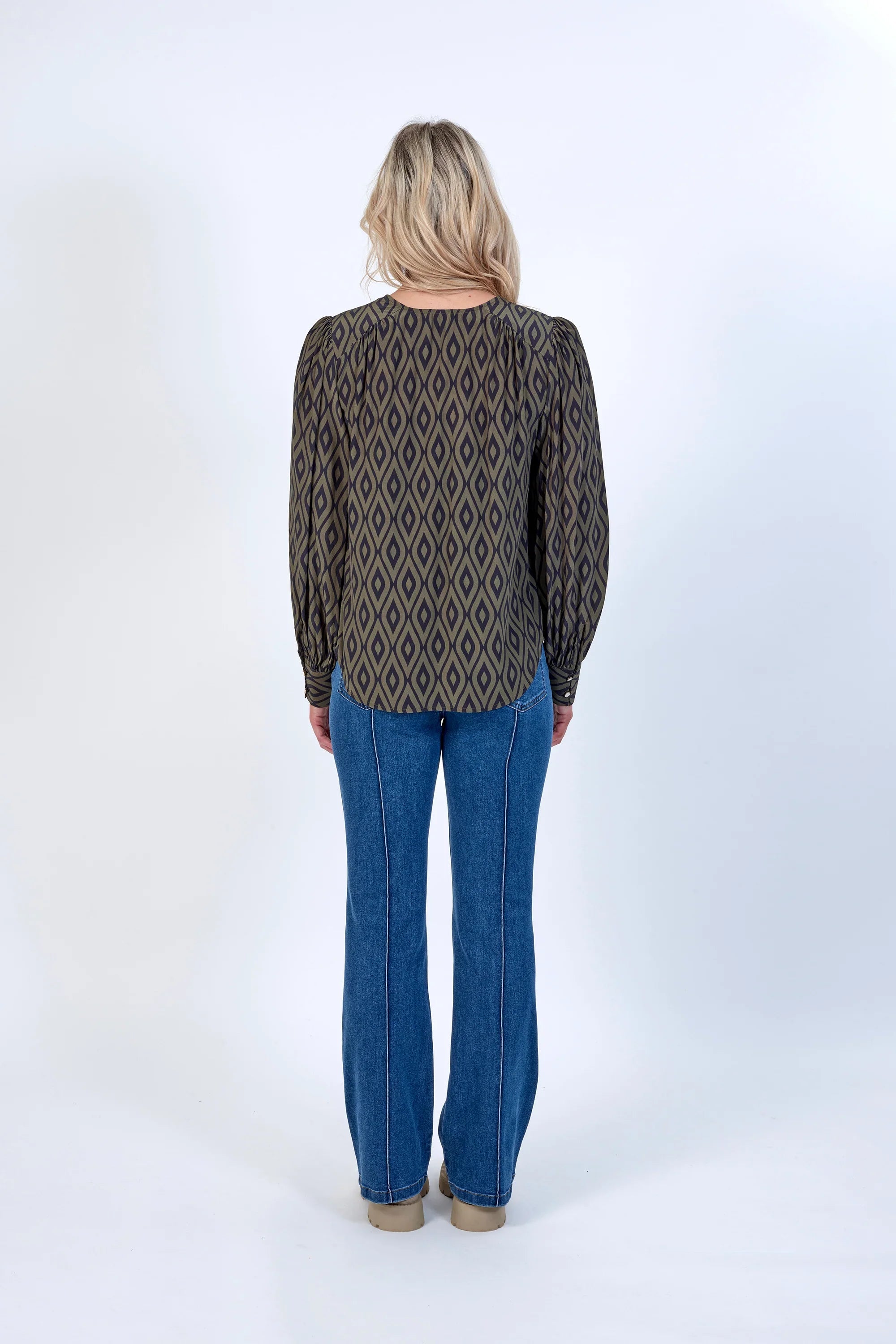 Woman wearing geometric print long sleeve blouse and blue jeans, back view, studio setting