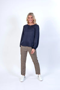 Woman wearing a navy long sleeve blouse and plaid pants with white sneakers, studio background