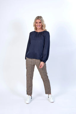 Woman wearing a navy long sleeve blouse and plaid pants with white sneakers, studio background