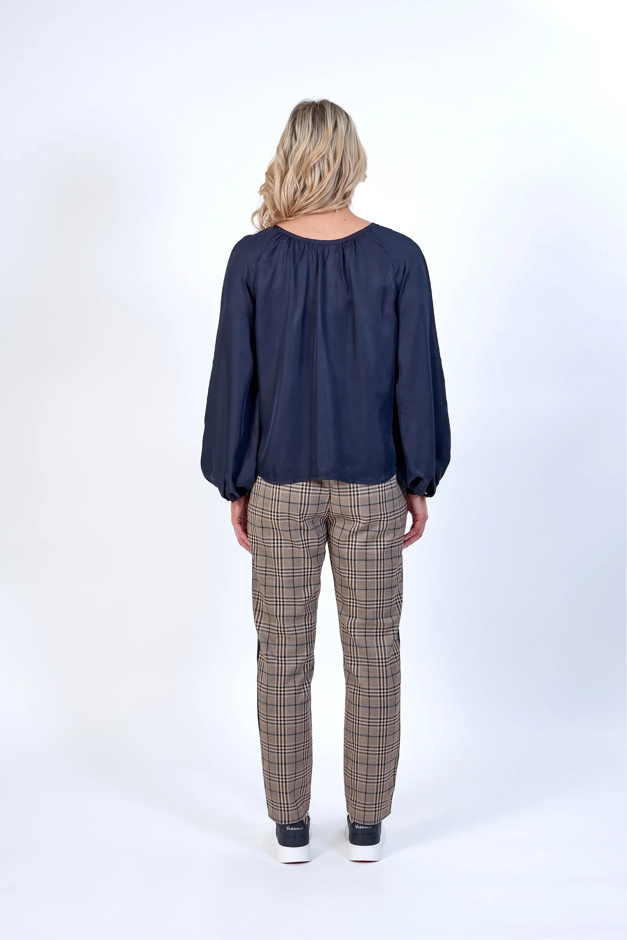 Woman wearing navy long sleeve blouse and plaid pants, back view, studio setting