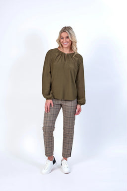 Woman wearing khaki long sleeve blouse and plaid pants, standing in studio with white background