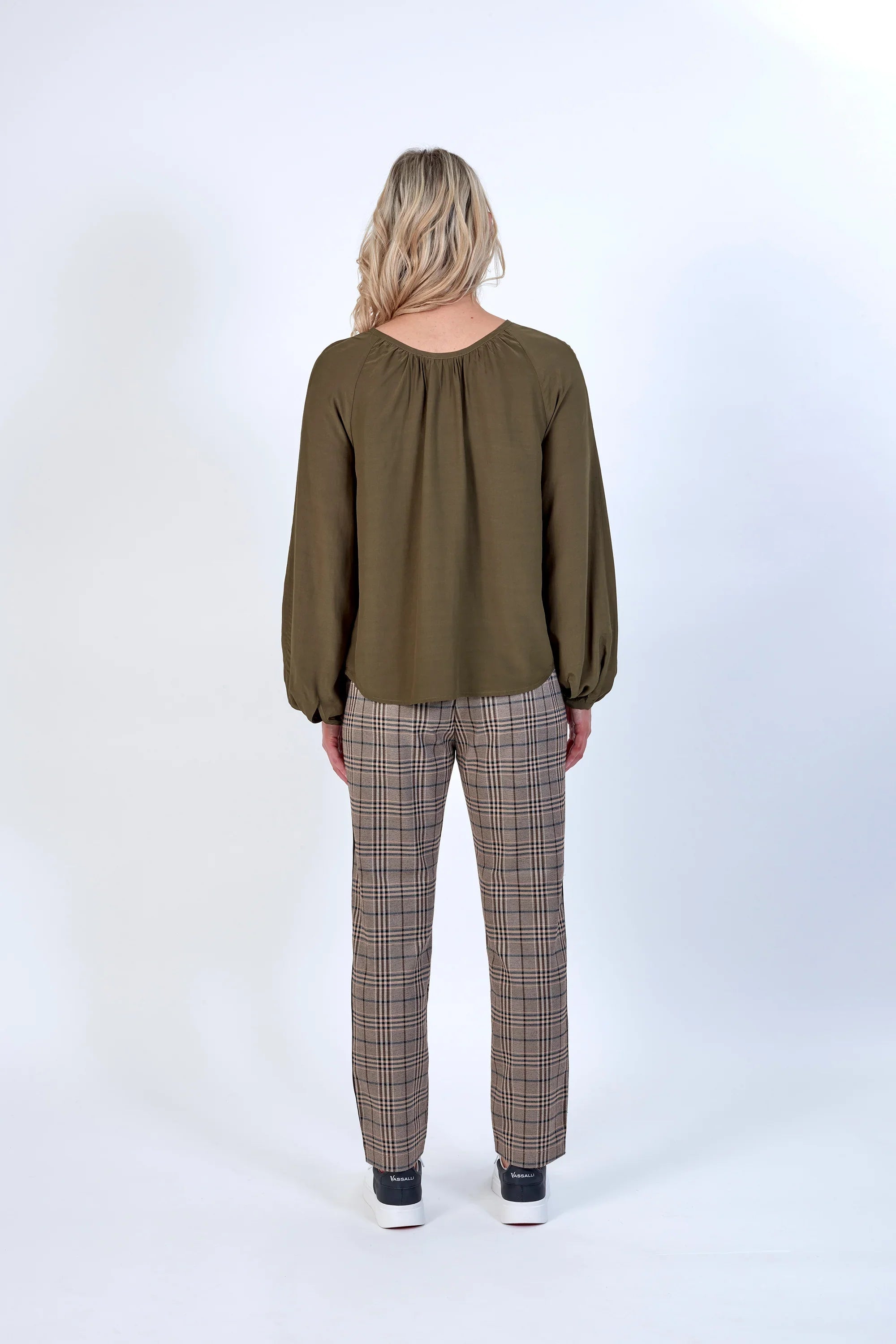 Back view of woman wearing khaki long sleeve blouse and plaid trousers