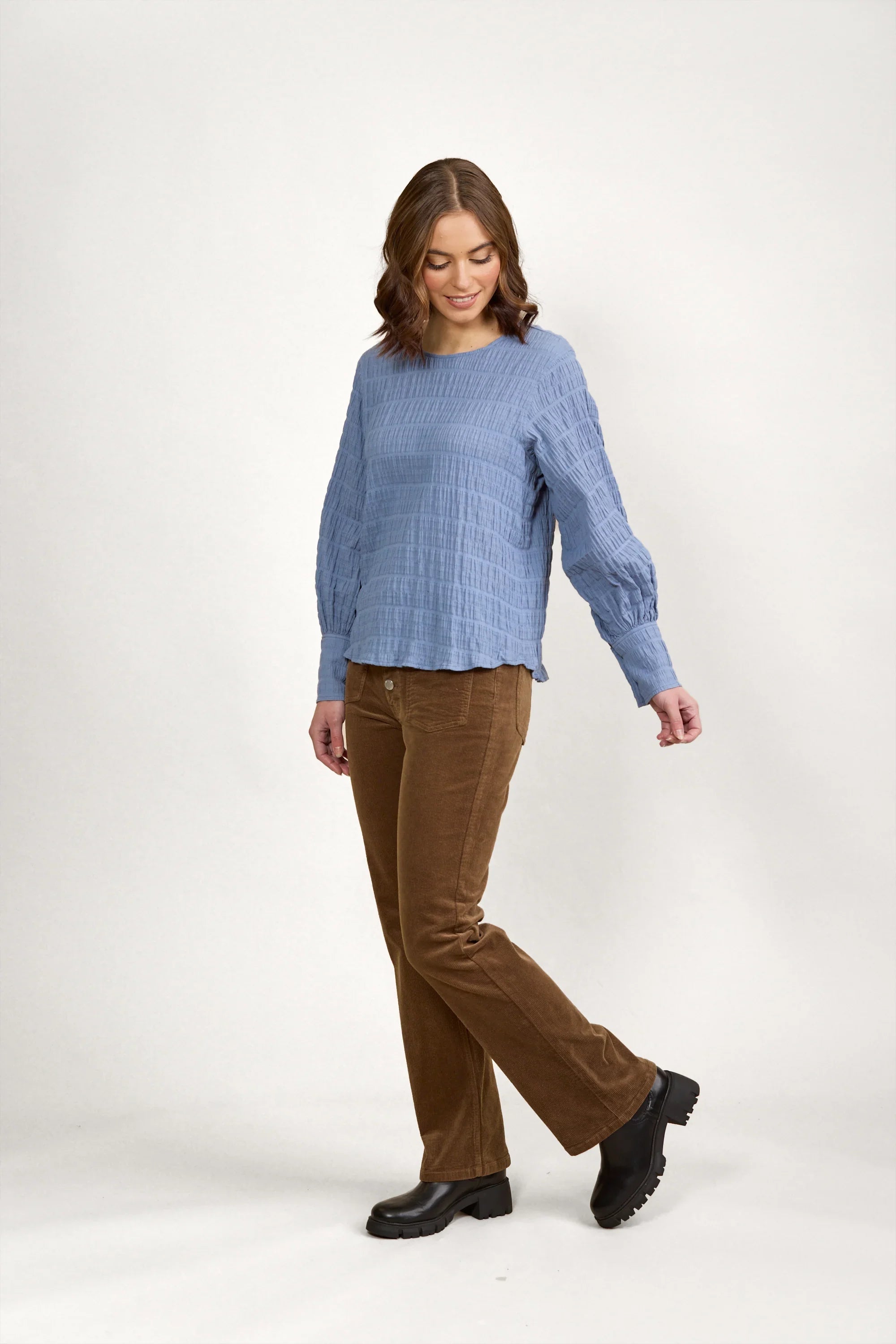 Woman wearing a textured blue volume top with long sleeves and brown corduroy pants