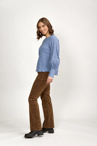 Woman in textured denim blue long sleeve top, brown corduroy pants, and black boots