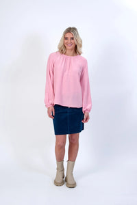 Woman wearing a light pink long sleeve top, blue skirt, and beige boots on white background