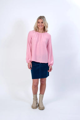 Woman wearing a light pink long sleeve top, blue skirt, and beige boots on white background