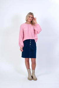 Woman wearing a light pink long sleeve blouse, blue corduroy skirt, and beige boots