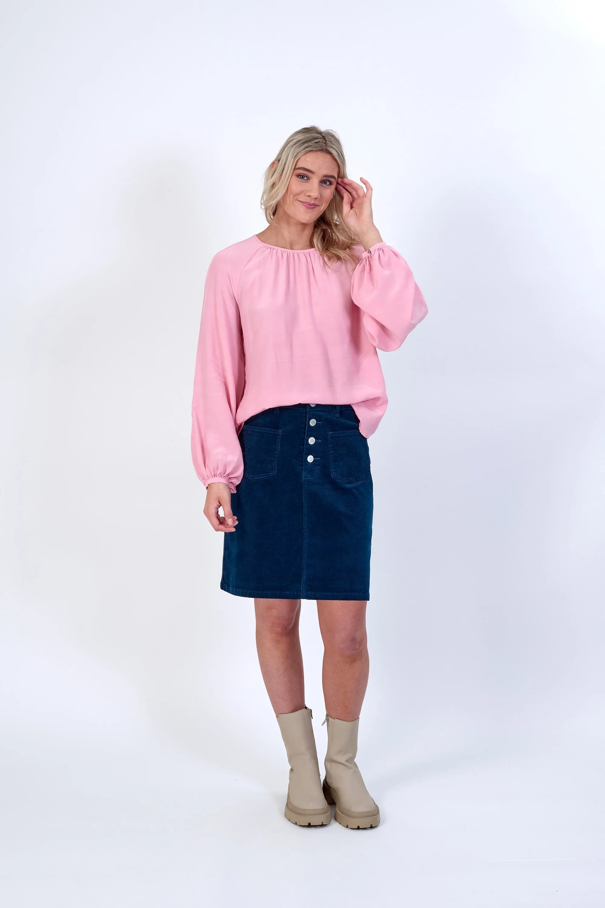 Woman wearing a light pink long sleeve blouse, blue corduroy skirt, and beige boots