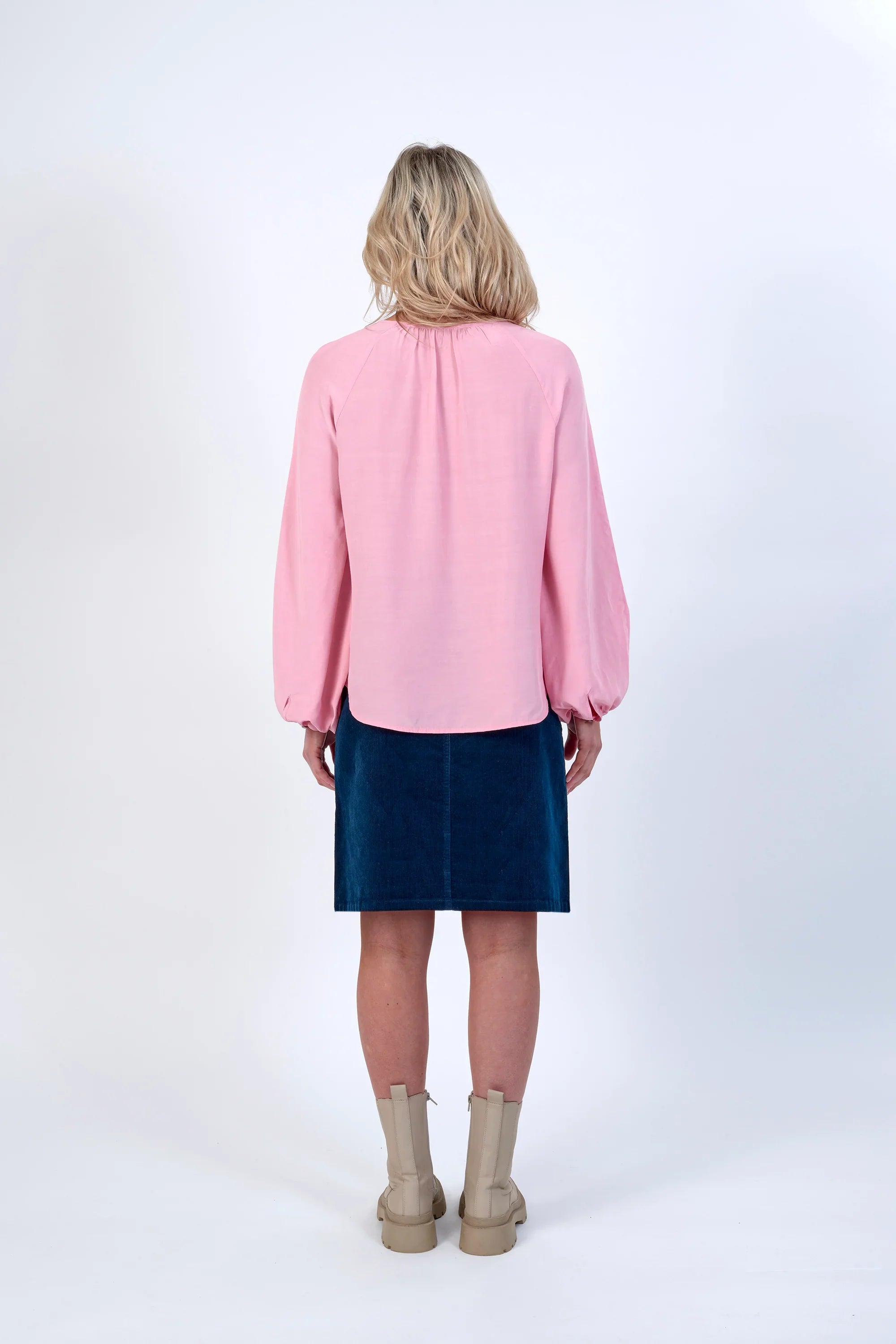 Woman wearing a pink long sleeve blouse, blue denim skirt, and beige boots, back view