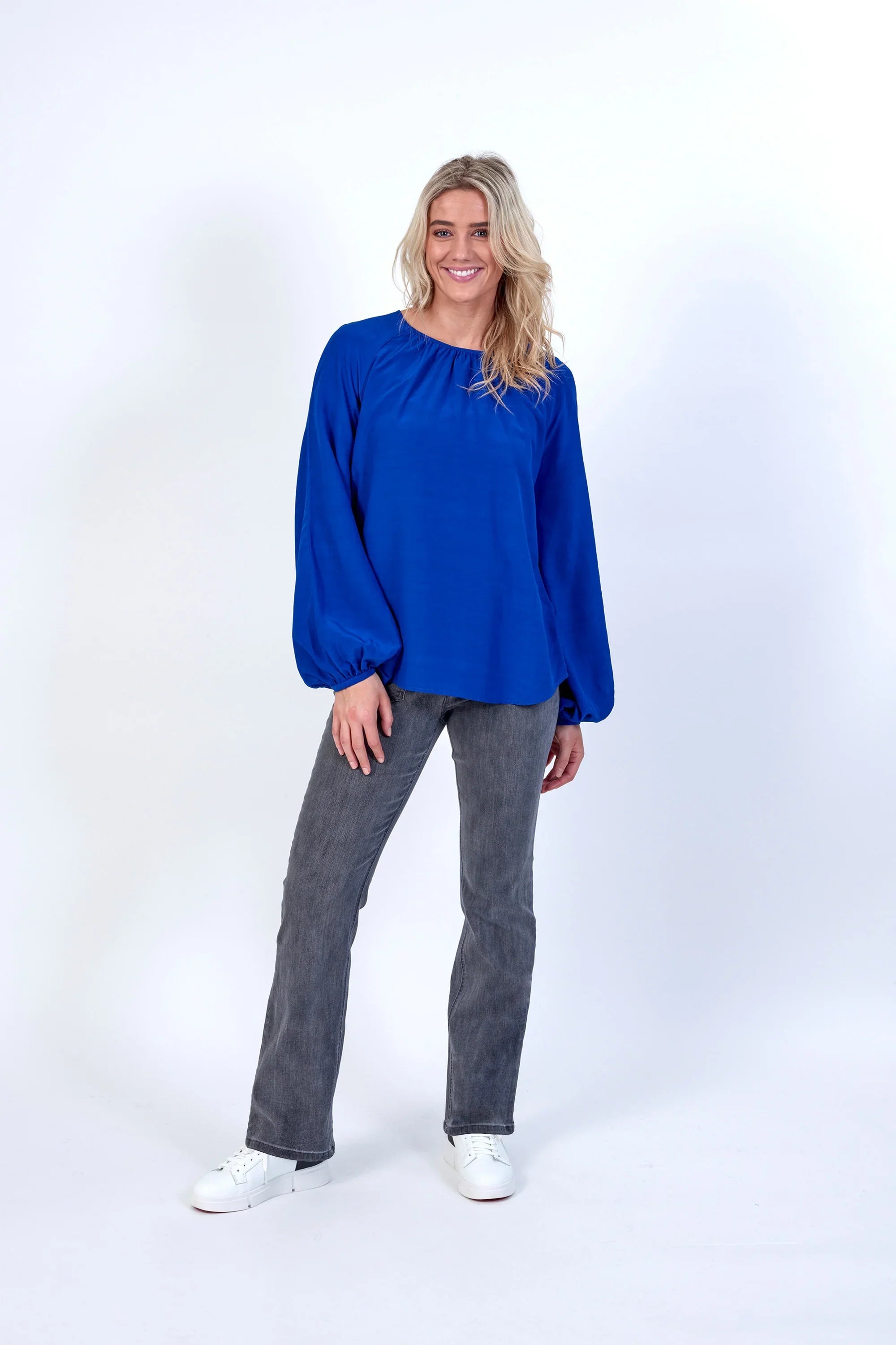 Woman wearing electric blue long sleeve blouse with grey jeans and white sneakers