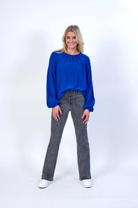 Woman wearing electric blue long sleeve blouse with grey high-waisted jeans and white sneakers