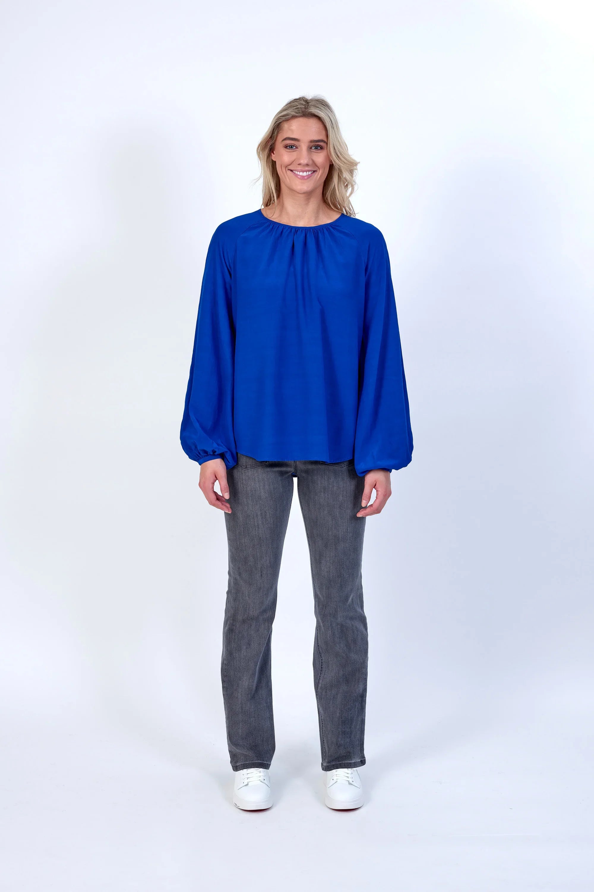 Woman wearing a bright blue long sleeve blouse with grey jeans and white shoes
