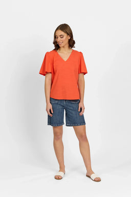 Woman wearing a melon orange V-neck flutter sleeve top with denim shorts and sandals