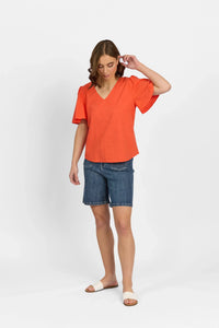 Woman wearing orange V-neck short sleeve blouse with denim shorts and slide sandals