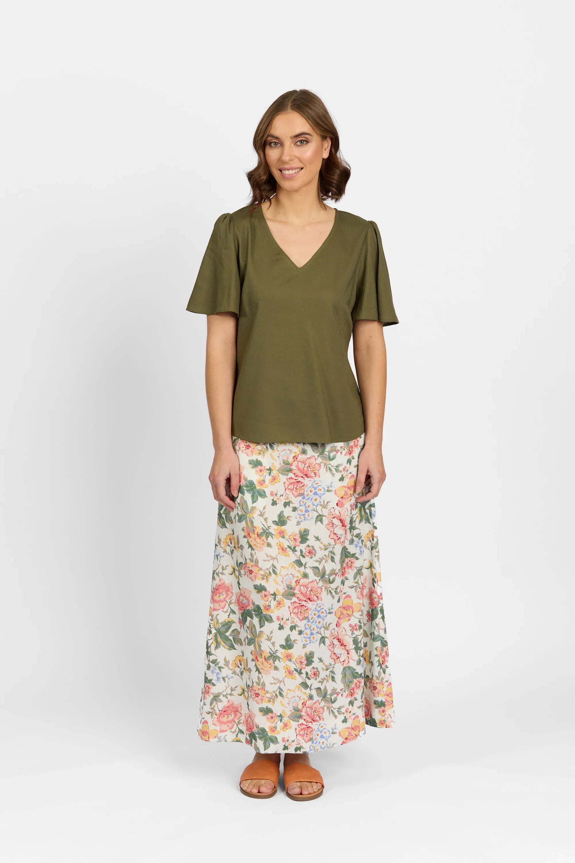 Woman in olive short sleeve V-neck blouse and floral print maxi skirt, standing against white background