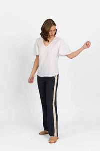 Woman wearing a white V-neck short sleeve top with black pants featuring beige side stripes