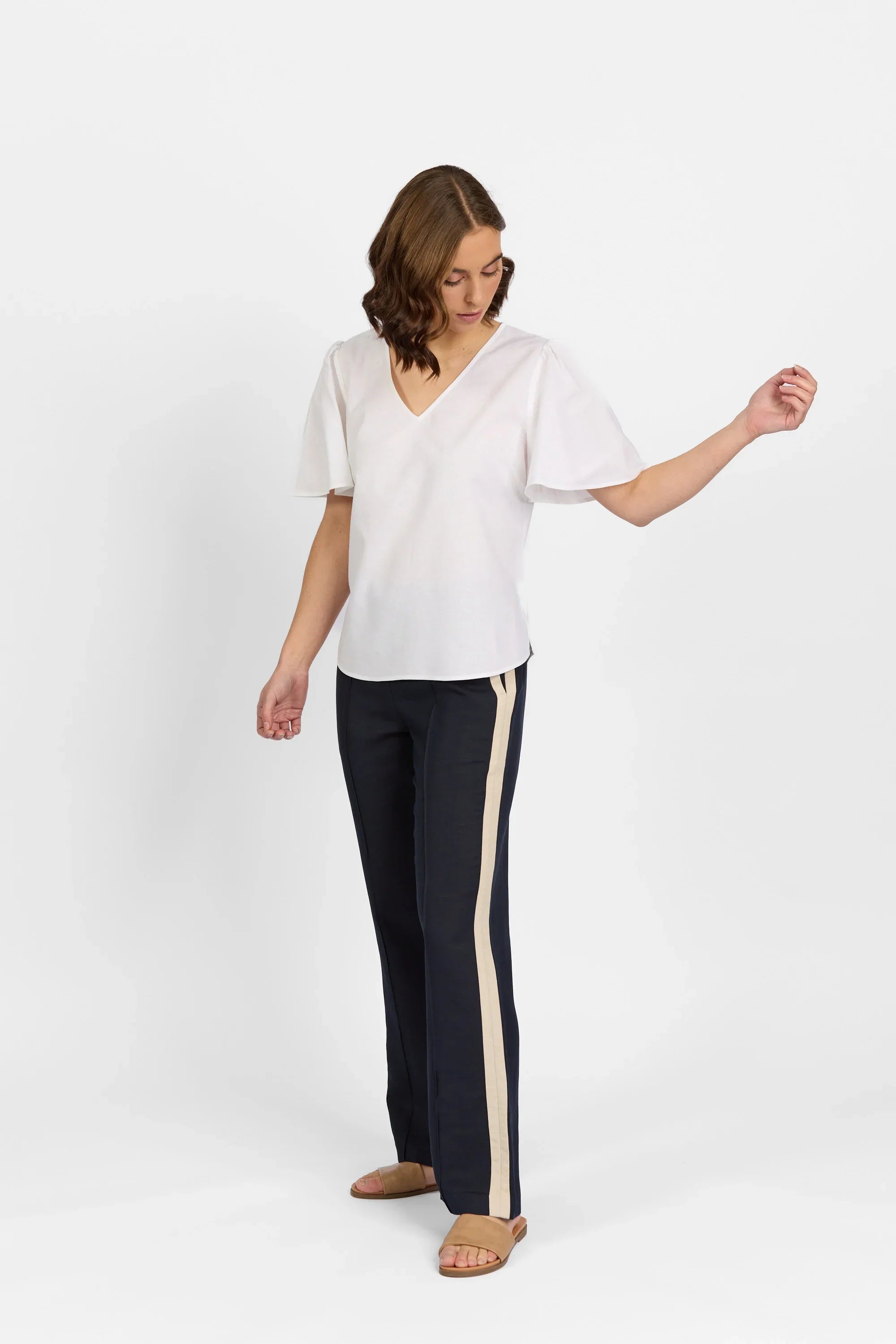 Woman wearing a white V-neck short sleeve top with black pants featuring beige side stripes