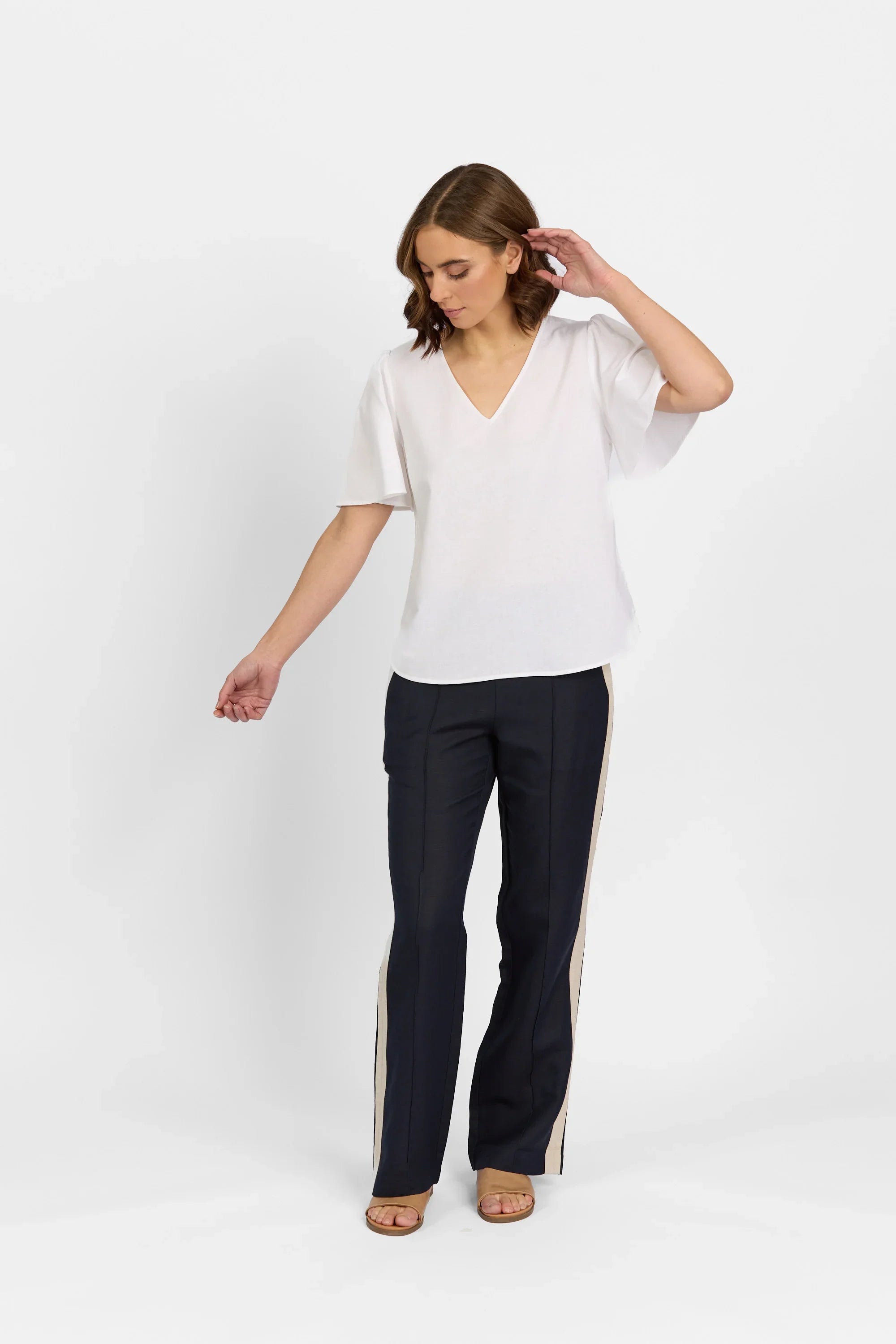 Woman modeling a white V-neck short sleeve top with navy pants featuring beige side stripes