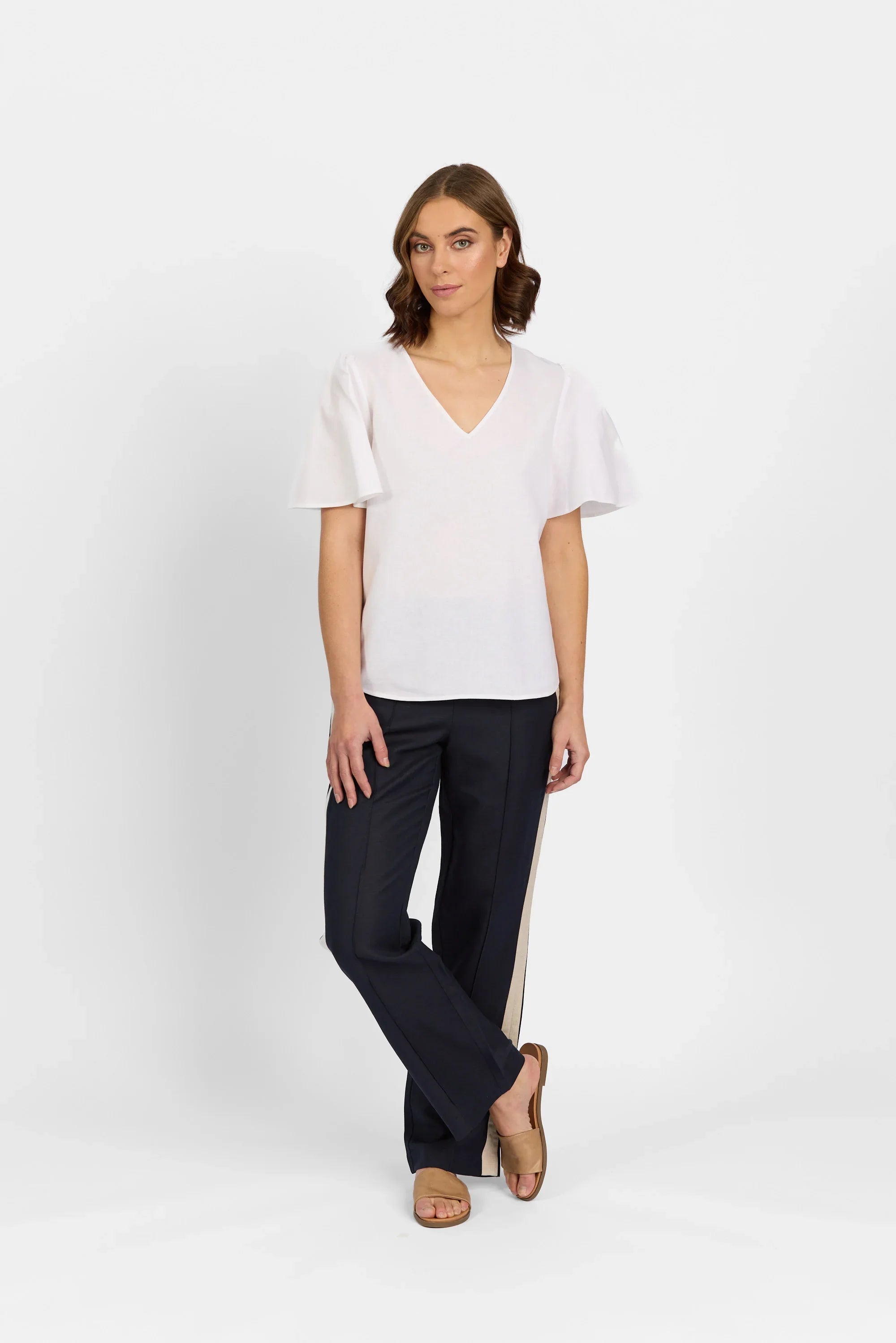 Woman wearing a white V-neck ruffle sleeve top and navy trousers with tan sandals
