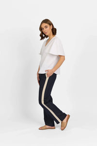 Woman wearing white flutter sleeve top and navy pants with beige stripe on white background