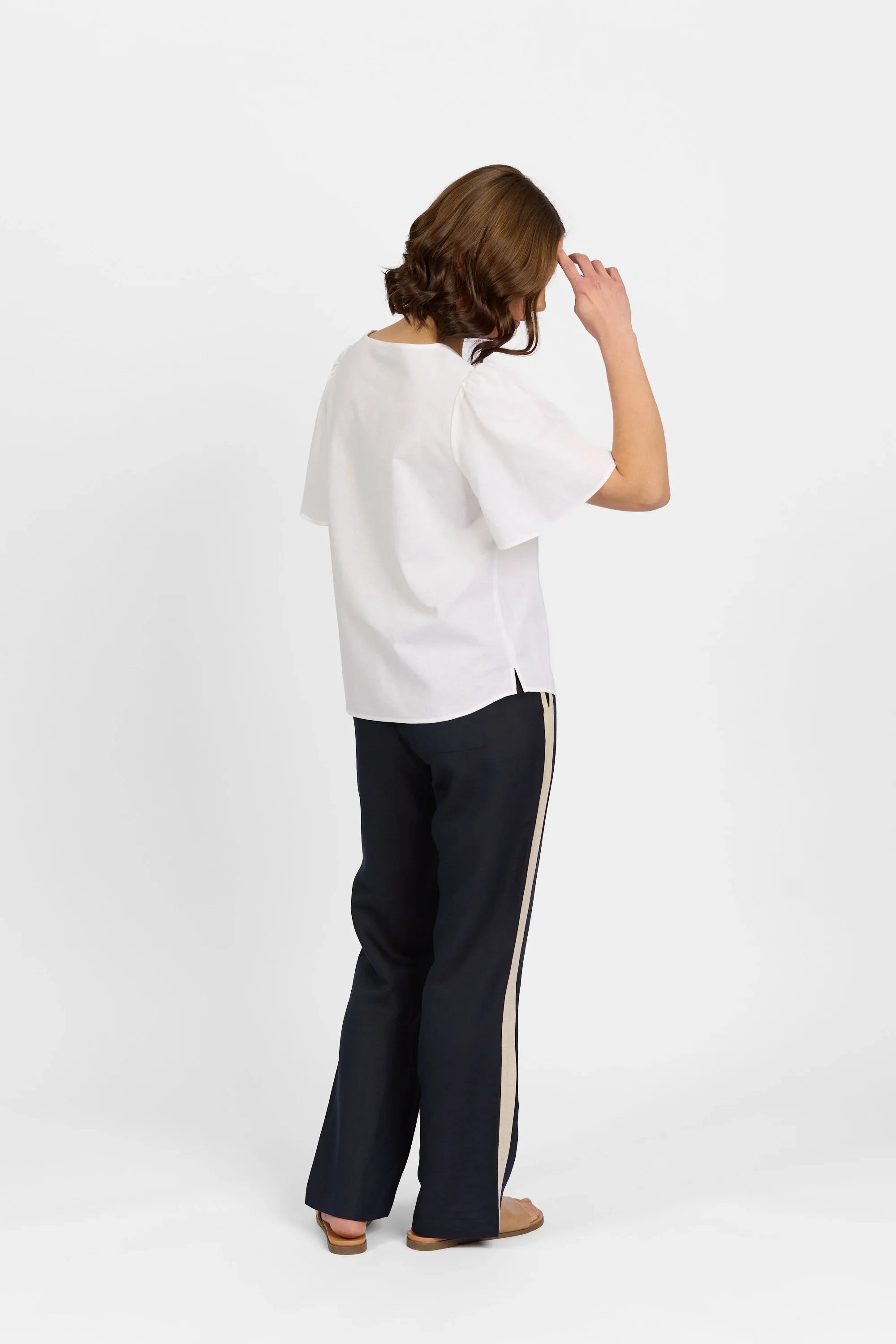 Woman wearing a white short-sleeve blouse and black wide-leg pants with beige side stripe