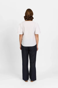Woman wearing white short sleeve top and black wide leg pants, back view on white background