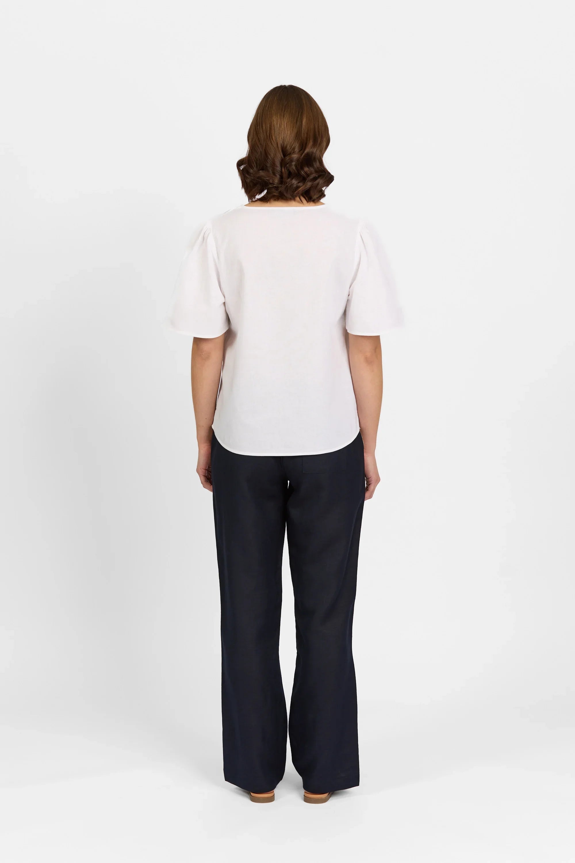 Woman wearing white short sleeve top and black wide leg pants, back view on white background