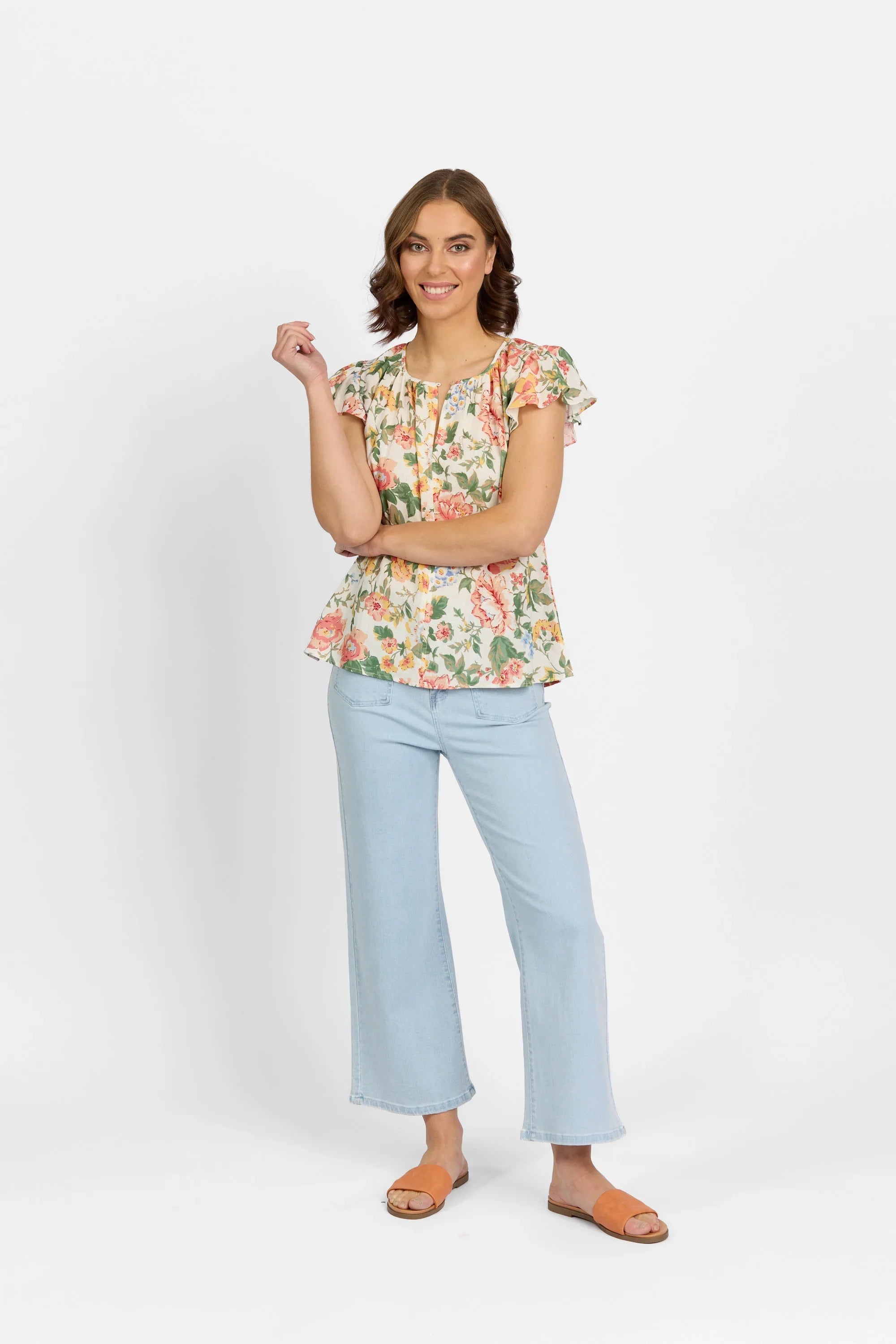 Woman wearing a floral short sleeve blouse with ruffle details, light blue wide-leg jeans, and orange sandals.