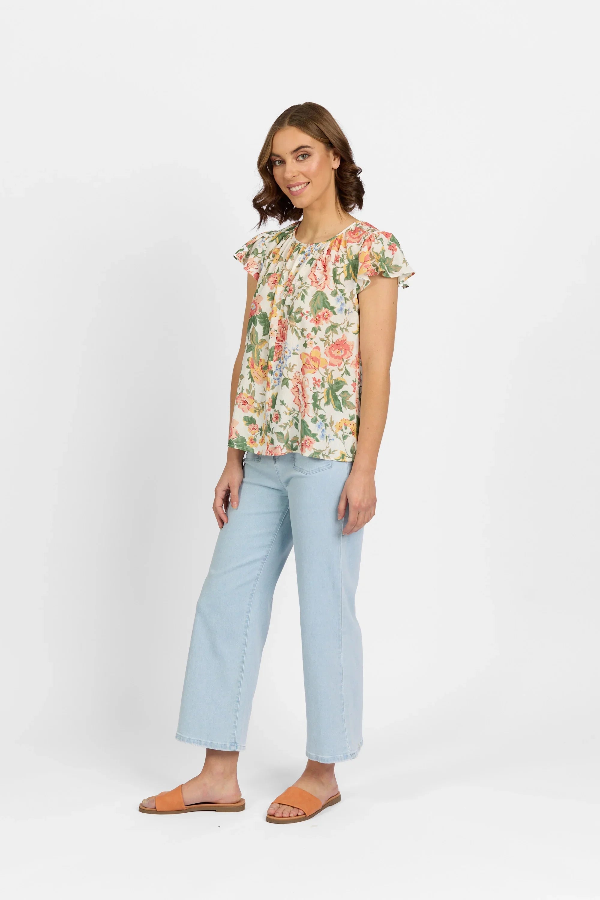 Woman in floral flutter sleeve top, light blue wide-leg jeans, and tan sandals