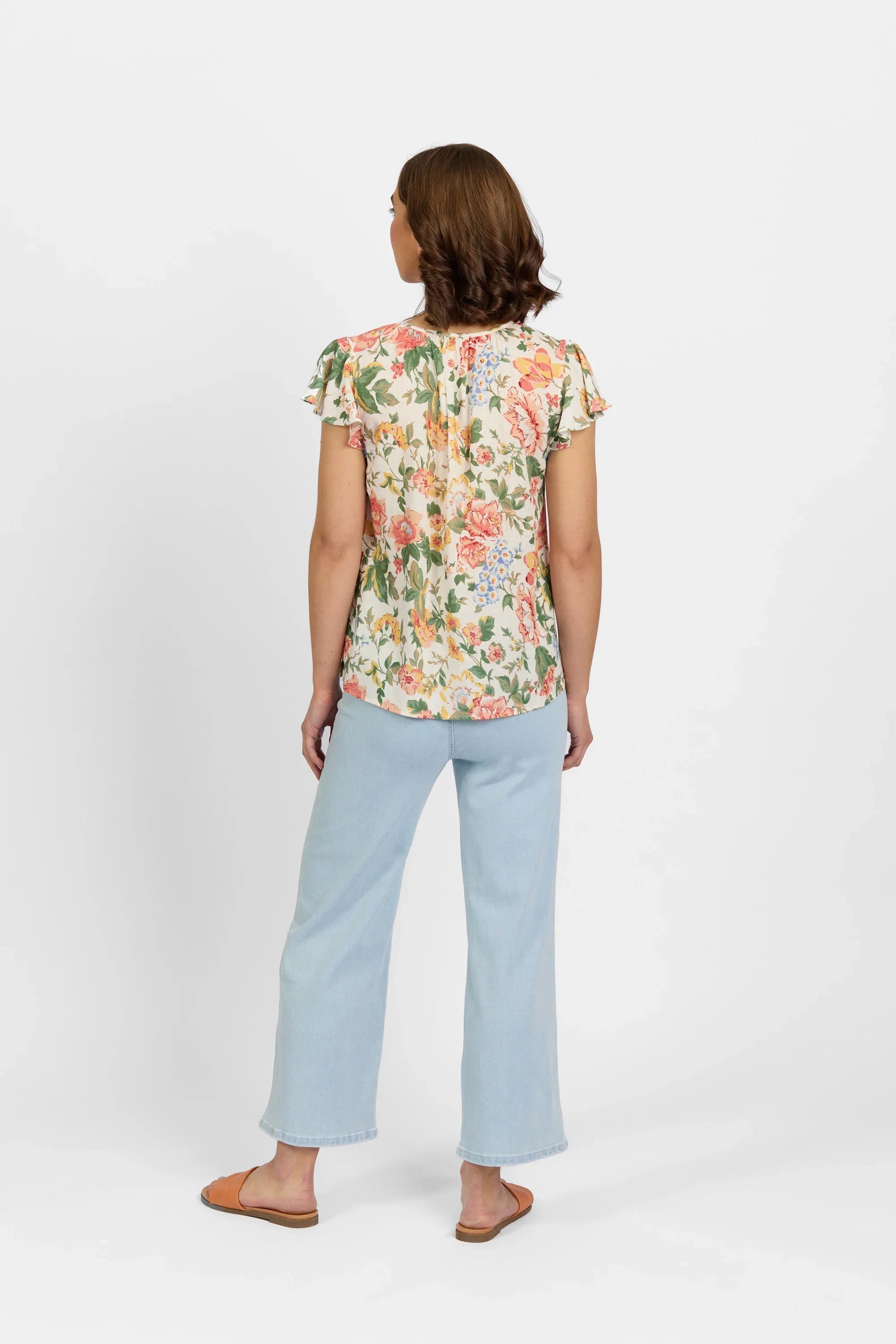 Woman in floral short sleeve top and light blue jeans, photographed from the back